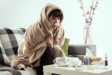 Image showing Woman wrapped in a plaid looks sick, ill, sneezing and coughing sitting at home indoors