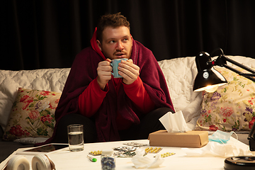 Image showing Man wrapped in a plaid looks sick, ill, sneezing and coughing sitting at home indoors