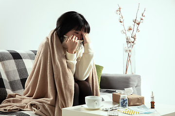 Image showing Woman wrapped in a plaid looks sick, ill, sneezing and coughing sitting at home indoors