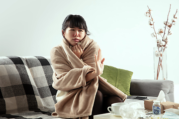 Image showing Woman wrapped in a plaid looks sick, ill, sneezing and coughing sitting at home indoors