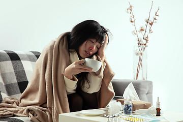 Image showing Woman wrapped in a plaid looks sick, ill, sneezing and coughing sitting at home indoors