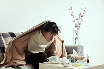 Image showing Woman wrapped in a plaid looks sick, ill, sneezing and coughing sitting at home indoors