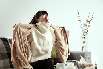 Image showing Woman wrapped in a plaid looks sick, ill, sneezing and coughing sitting at home indoors