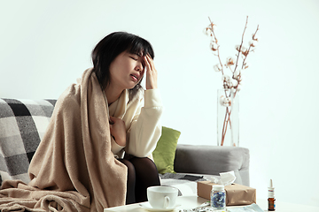 Image showing Woman wrapped in a plaid looks sick, ill, sneezing and coughing sitting at home indoors