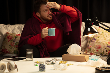 Image showing Man wrapped in a plaid looks sick, ill, sneezing and coughing sitting at home indoors