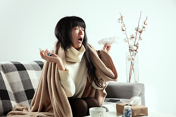 Image showing Woman wrapped in a plaid looks sick, ill, sneezing and coughing sitting at home indoors