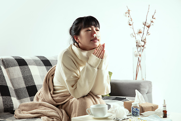 Image showing Woman wrapped in a plaid looks sick, ill, sneezing and coughing sitting at home indoors