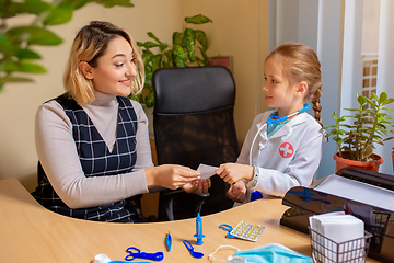 Image showing Paediatrician doctor examining a child in comfortabe medical office. Little girl playing pretends like doctor for woman