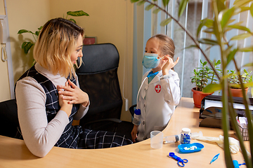 Image showing Paediatrician doctor examining a child in comfortabe medical office. Little girl playing pretends like doctor for woman