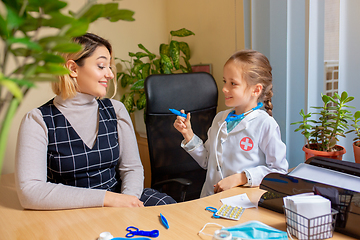 Image showing Paediatrician doctor examining a child in comfortabe medical office. Little girl playing pretends like doctor for woman