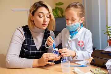 Image showing Paediatrician doctor examining a child in comfortabe medical office. Little girl playing pretends like doctor for woman