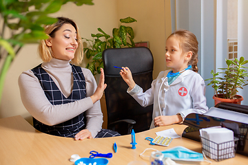 Image showing Paediatrician doctor examining a child in comfortabe medical office. Little girl playing pretends like doctor for woman