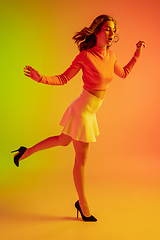 Image showing Beautiful seductive girl in fashionable, romantic outfit on bright gradient green-orange background in neon light