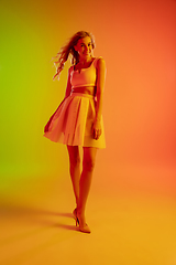 Image showing Beautiful seductive girl in fashionable, romantic outfit on bright gradient green-orange background in neon light