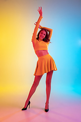 Image showing Beautiful seductive girl in fashionable, romantic yellow outfit on bright gradient yellow-blue background in neon light