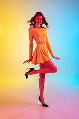 Image showing Beautiful seductive girl in fashionable, romantic yellow outfit on bright gradient yellow-blue background in neon light