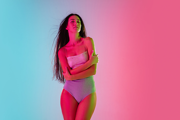 Image showing Beautiful seductive girl in fashionable swimsuit on bright gradient pink-blue background in neon light
