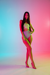 Image showing Beautiful seductive girl in fashionable swimsuit on bright gradient pink-blue background in neon light