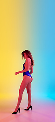 Image showing Beautiful seductive girl in fashionable blue swimsuit on bright gradient yellow-blue background in neon light