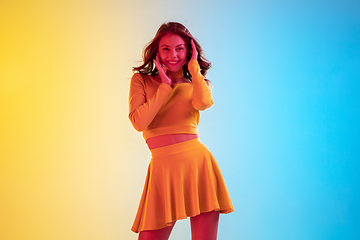 Image showing Beautiful seductive girl in fashionable, romantic yellow outfit on bright gradient yellow-blue background in neon light