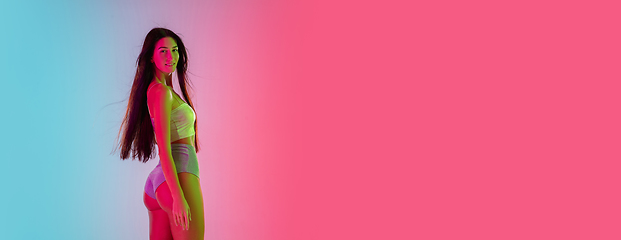 Image showing Beautiful seductive girl in fashionable swimsuit on bright gradient pink-blue background in neon light