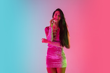 Image showing Beautiful seductive girl in fashionable dress, outfit on bright gradient pink-blue background in neon light