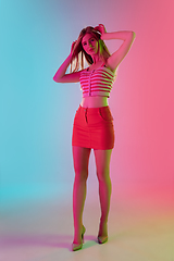 Image showing Beautiful girl in fashionable, romantic outfit on bright gradient pink-blue background in neon light