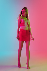 Image showing Beautiful girl in fashionable, romantic outfit on bright gradient pink-blue background in neon light