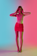 Image showing Beautiful girl in fashionable, romantic outfit on bright gradient pink-blue background in neon light