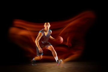 Image showing Young east asian basketball player in action and jump in mixed light over dark studio background. Concept of sport, movement, energy and dynamic, healthy lifestyle.