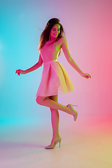 Image showing Beautiful seductive girl in fashionable, romantic outfit on bright gradient pink-blue background in neon light