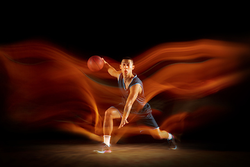 Image showing Young east asian basketball player in action and jump in mixed light over dark studio background. Concept of sport, movement, energy and dynamic, healthy lifestyle.