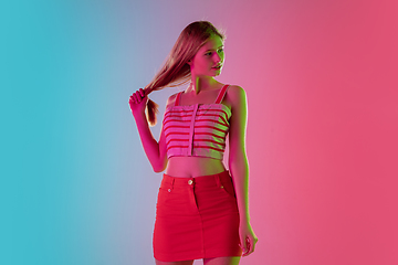 Image showing Beautiful girl in fashionable, romantic outfit on bright gradient pink-blue background in neon light