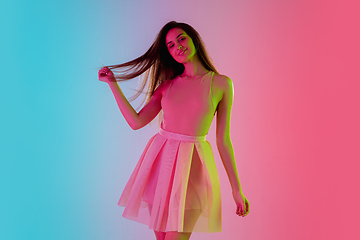 Image showing Beautiful seductive girl in fashionable, romantic outfit on bright gradient pink-blue background in neon light