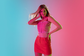 Image showing Beautiful girl in fashionable, romantic outfit on bright gradient pink-blue background in neon light