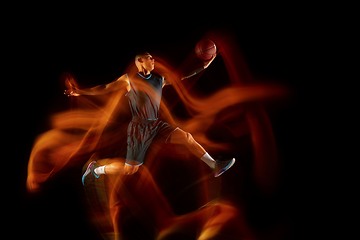 Image showing Young east asian basketball player in action and jump in mixed light over dark studio background. Concept of sport, movement, energy and dynamic, healthy lifestyle.