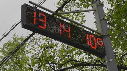Image showing Street electronic clock on the table in the foliage of a tree.