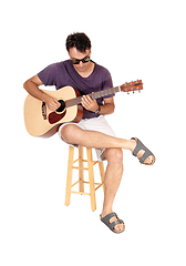 Image showing Young man sitting and playing his guitar