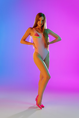 Image showing Beautiful seductive girl in fashionable pink swimsuit on bright gradient purple-blue background in neon light