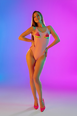 Image showing Beautiful seductive girl in fashionable pink swimsuit on bright gradient purple-blue background in neon light