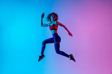 Image showing Young beautiful woman in bright sportwear isolated on gradient pink-blue studio background in neon light.