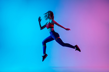 Image showing Young sportive woman running isolated on gradient pink-blue studio background in neon light.