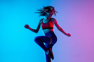 Image showing Sportive young happy woman in bright sportwear isolated on gradient pink-blue studio background in neon light.