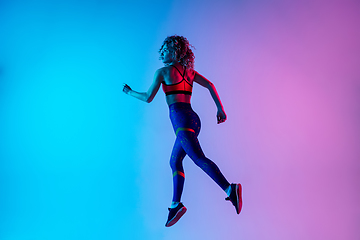 Image showing Young sportive woman running isolated on gradient pink-blue studio background in neon light.