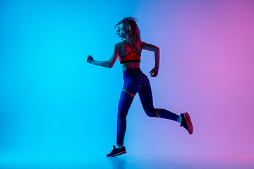 Image showing Young sportive woman running isolated on gradient pink-blue studio background in neon light.