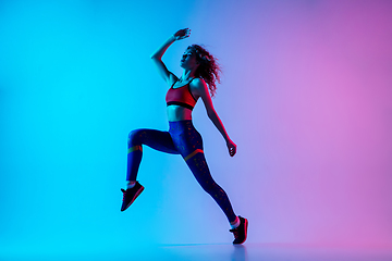 Image showing Young sportive woman running isolated on gradient pink-blue studio background in neon light.