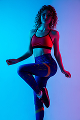 Image showing Young sportive woman training isolated on gradient pink-blue studio background in neon light.