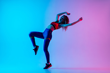 Image showing Sportive young happy woman in bright sportwear isolated on gradient pink-blue studio background in neon light.