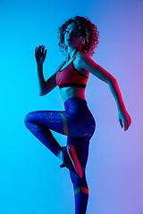 Image showing Young sportive woman training isolated on gradient pink-blue studio background in neon light.