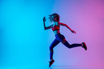 Image showing Young sportive woman running isolated on gradient pink-blue studio background in neon light.